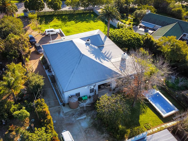Aerial view of the property featuring a metal roof, swimming pool, and surrounding garden area with driveway access.