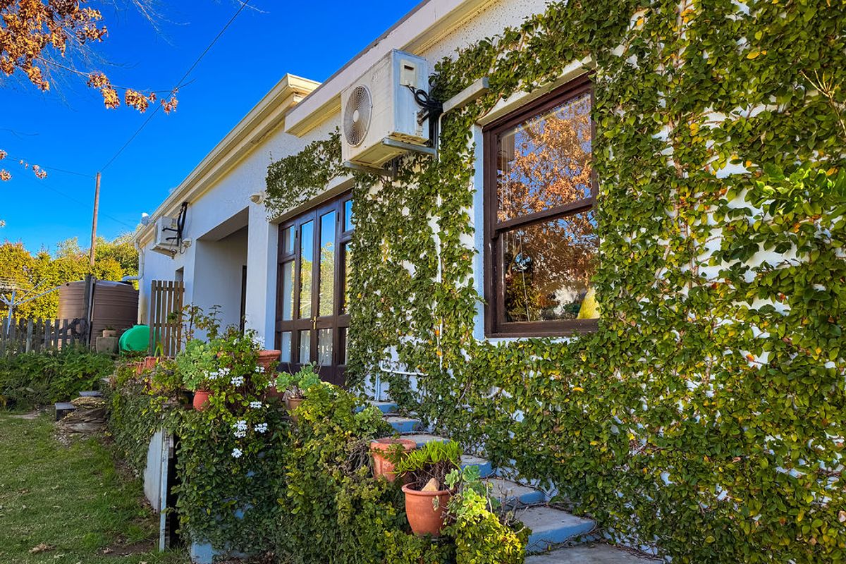 Rear exterior view of the property featuring climbing ivy, timber-framed windows and doors, and an installed air conditioning unit.