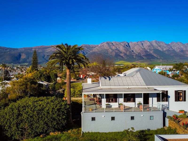Aerial view of a residential property featuring a metal roof, covered veranda, and scenic mountain backdrop.