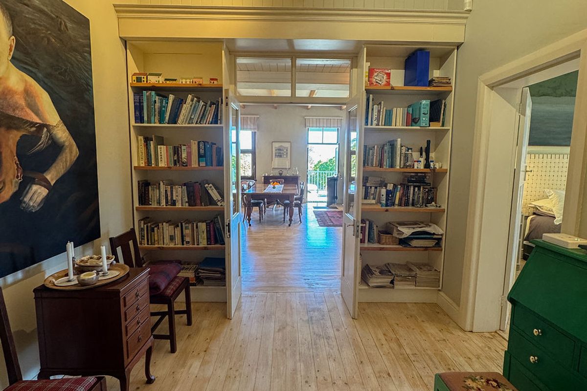 A bright living area featuring polished timber flooring, high tongue and groove ceilings, and custom built-in bookshelves framing the entrance to the dining room.