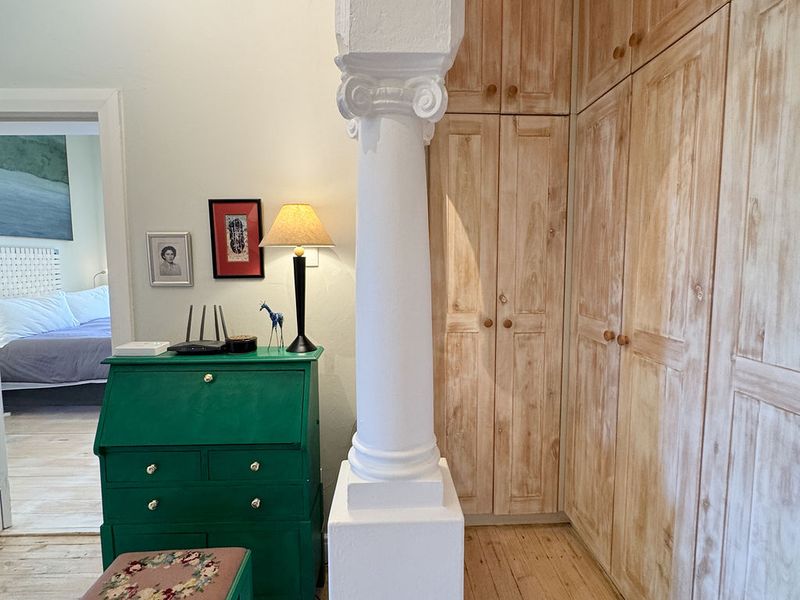 A bedroom area featuring extensive built-in wooden cabinetry, a decorative architectural column, and light-toned hardwood flooring, leading into an adjacent sleeping space.