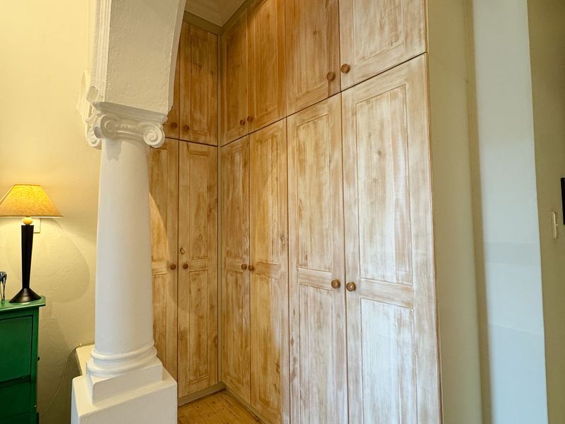 A bedroom featuring floor-to-ceiling built-in wooden cabinetry, complemented by a decorative archway with a classical column and warm timber flooring.