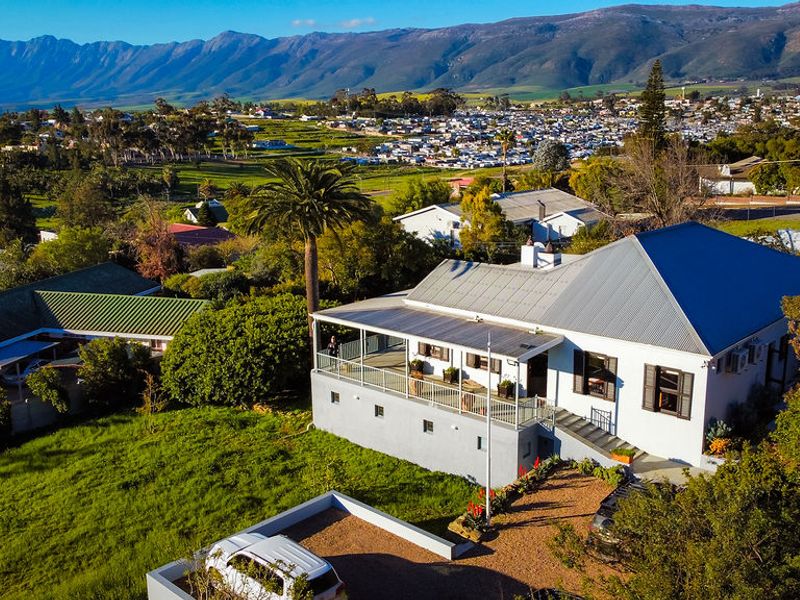 Aerial view of a residential property featuring a metal roof, a spacious covered veranda, and expansive garden grounds with mountain views.