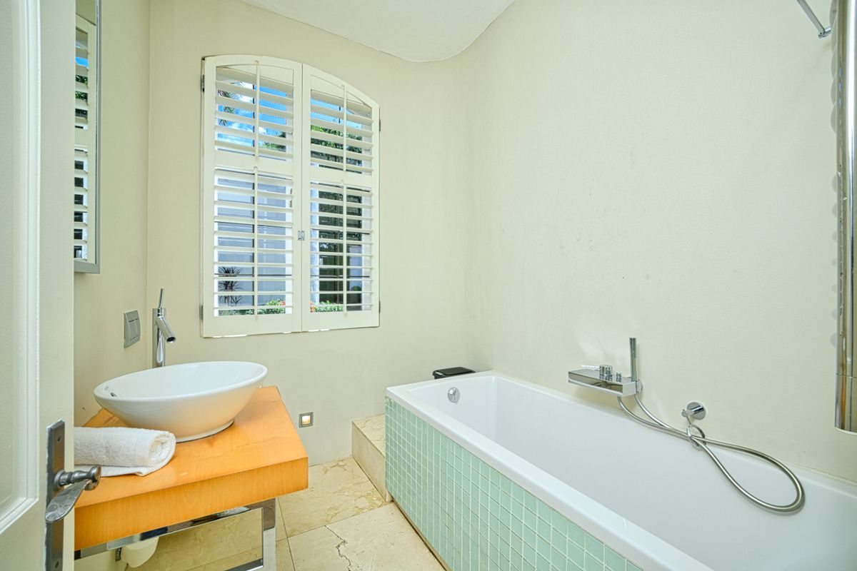 A well-maintained bathroom featuring a vessel sink on a floating vanity, a bathtub with a tiled apron, and plantation shutters.