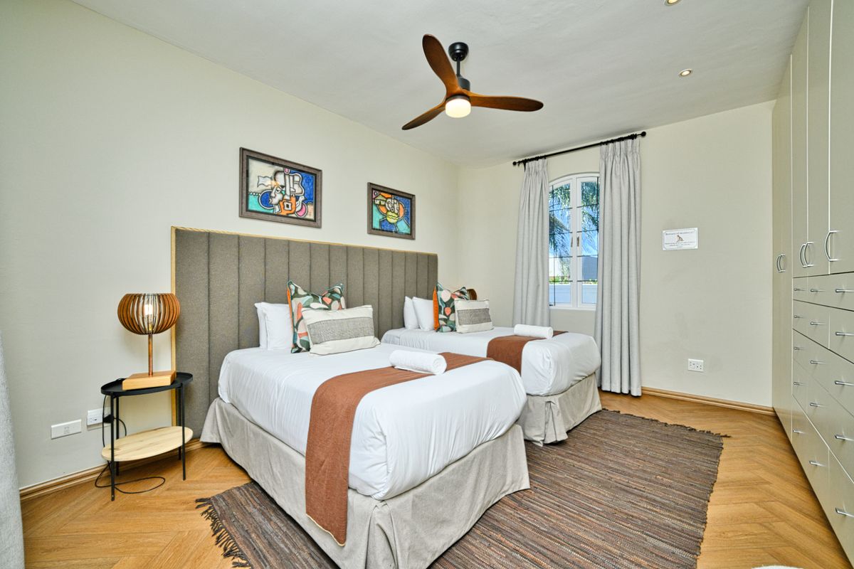 A well-maintained bedroom featuring herringbone flooring, built-in cupboards, a modern ceiling fan, and an arched window providing natural light.