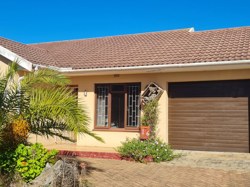 Front elevation of a single-story house featuring a double garage, tiled roof, and paved driveway with established garden.