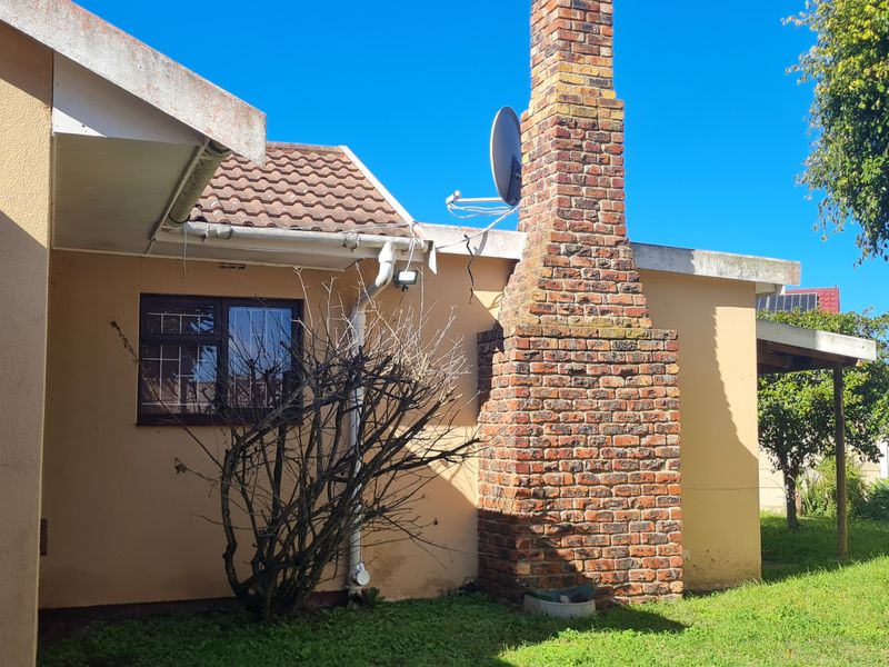 Rear exterior view of the property featuring a prominent brick chimney, concrete roof tiles, and a precast concrete boundary wall.