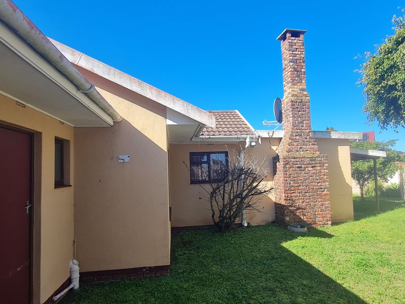 Rear exterior view of the property featuring a brick chimney, tiled roof, and a precast concrete boundary wall enclosing the garden area.
