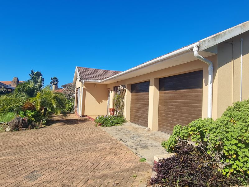 Front exterior view of the property featuring a double garage, paved driveway, and established garden area.