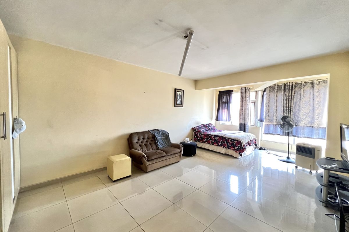 Spacious bedroom featuring large format floor tiles and a built-in wardrobe, requiring minor cosmetic updates to the ceiling and lighting.