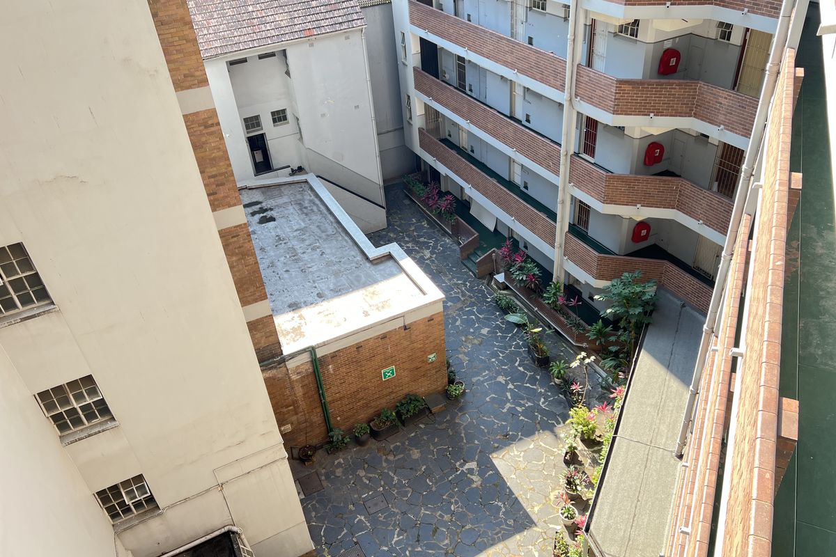 An elevated view of the apartment complex courtyard featuring paved flooring, brick building facades, and external balcony walkways with fire safety equipment.