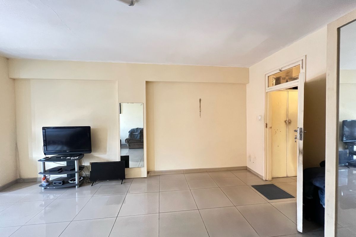 A living room area featuring large format floor tiles, a built-in wall mirror, and an internal door with a transom window.