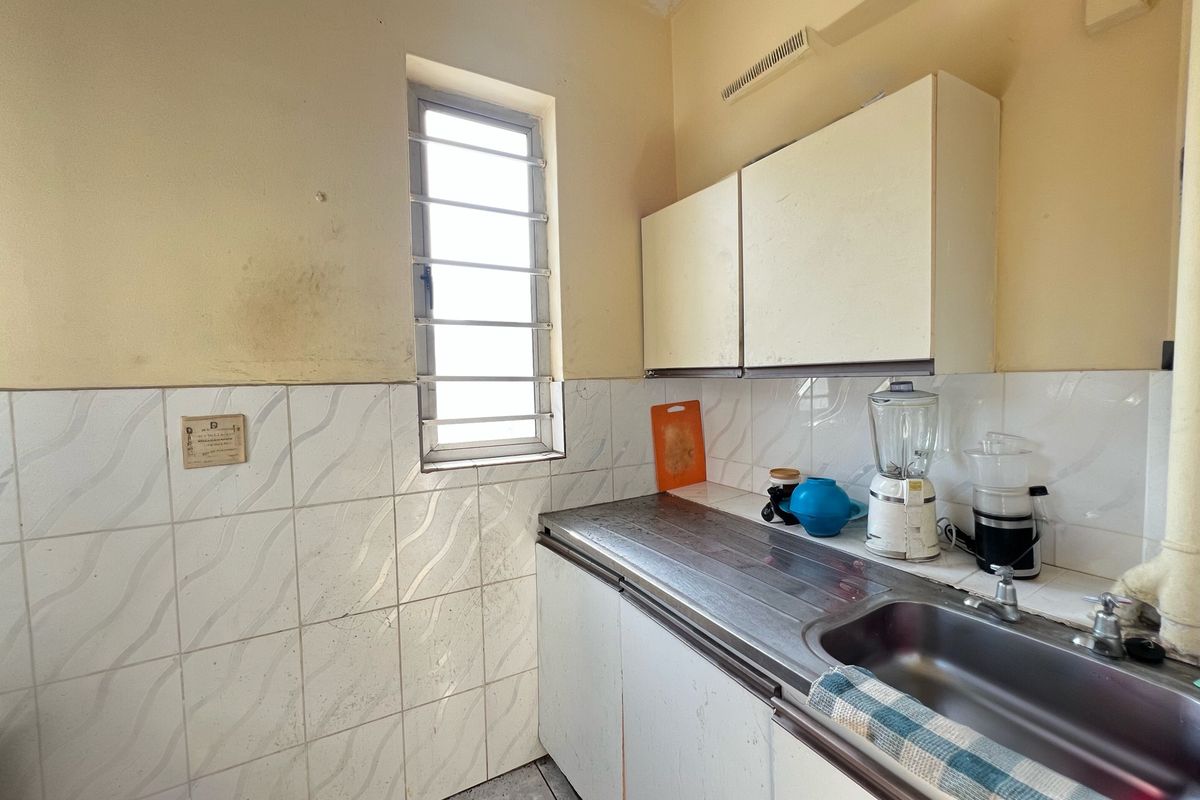 A compact kitchen area featuring a stainless steel sink, tiled splashback, and built-in cabinetry, requiring cosmetic updates to improve the overall aesthetic.