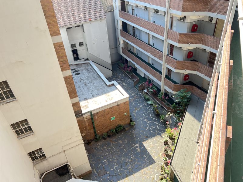 An elevated view of the apartment complex courtyard featuring paved flooring, brick building facades, and external balcony walkways with fire safety equipment.