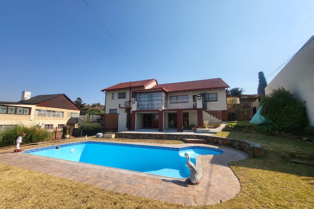 Rear view of a two-story house featuring a swimming pool with brick paving, a stone retaining wall, and an elevated balcony with metal railings.