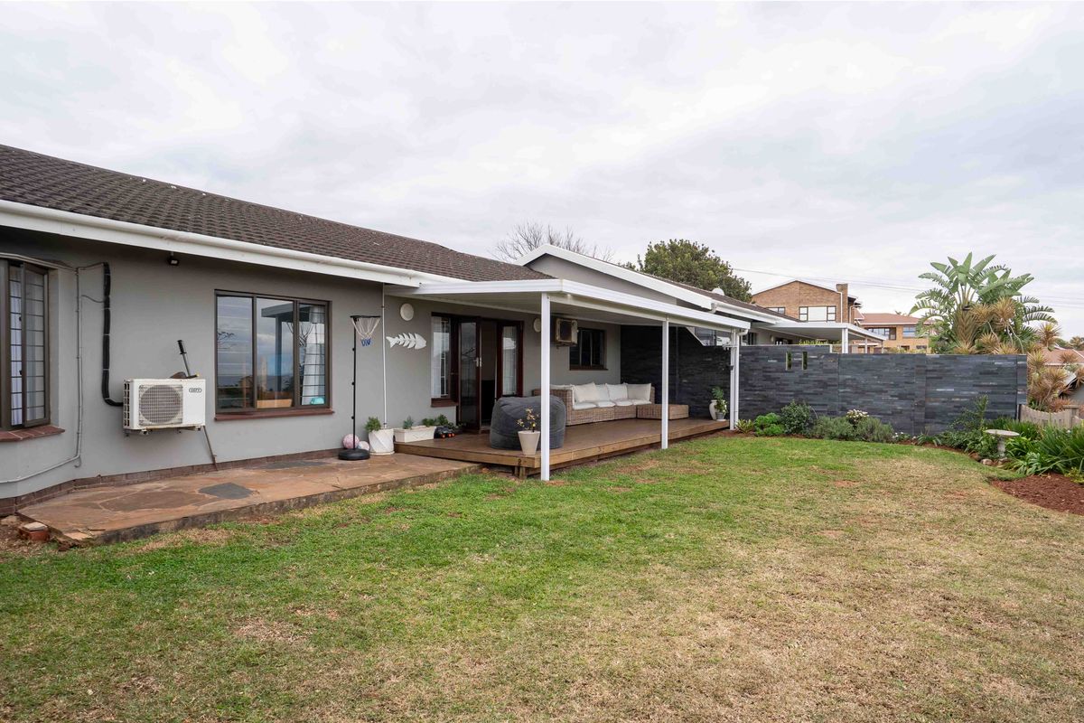 Rear view of the townhouse featuring a covered timber deck patio, stone feature wall, and a well-maintained garden area.