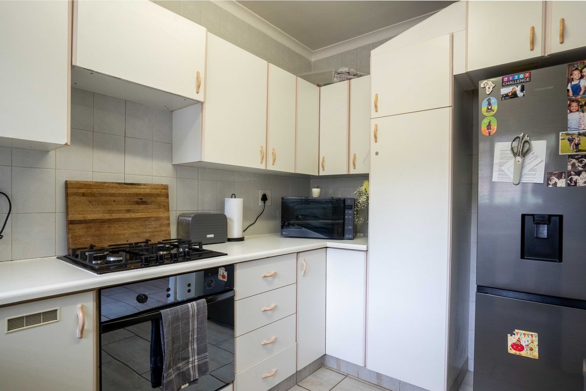 A functional kitchen featuring white cabinetry, a gas hob, built-in oven, and tiled backsplash, providing a practical workspace for daily cooking.