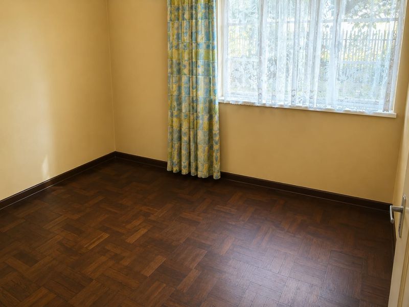 An empty bedroom featuring dark parquet flooring and neutral wall tones, providing a clean and versatile space ready for personalization.