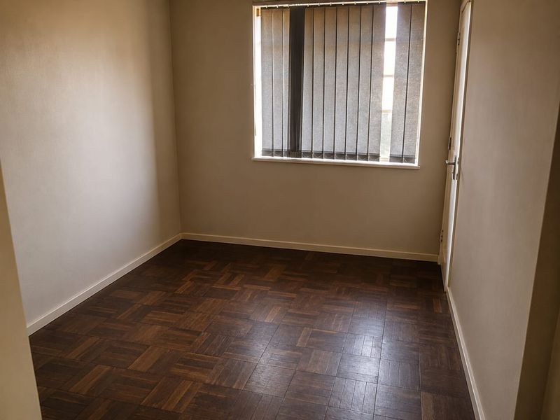 An empty bedroom featuring dark parquet flooring and vertical window blinds, offering a neutral canvas for interior design.