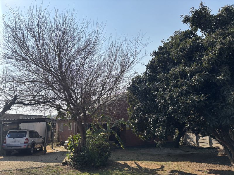 Front exterior view of the property featuring a paved driveway, carport, and established garden with mature trees.