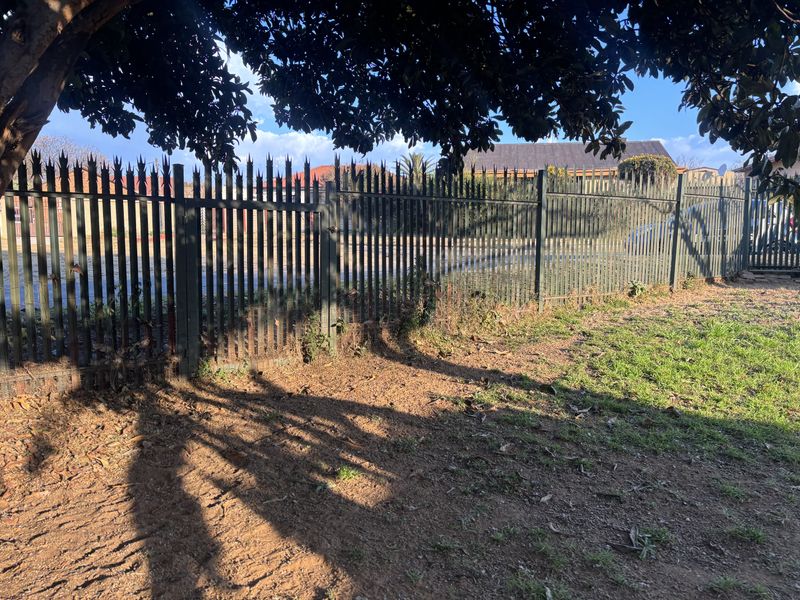A view of the property boundary featuring a metal spike fence and pedestrian gate, showing signs of weathering and rust.