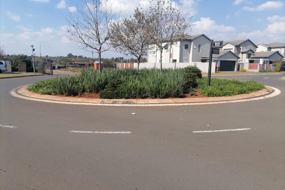 A view of a residential street roundabout featuring mature trees and landscaped garden beds within a suburban estate setting.