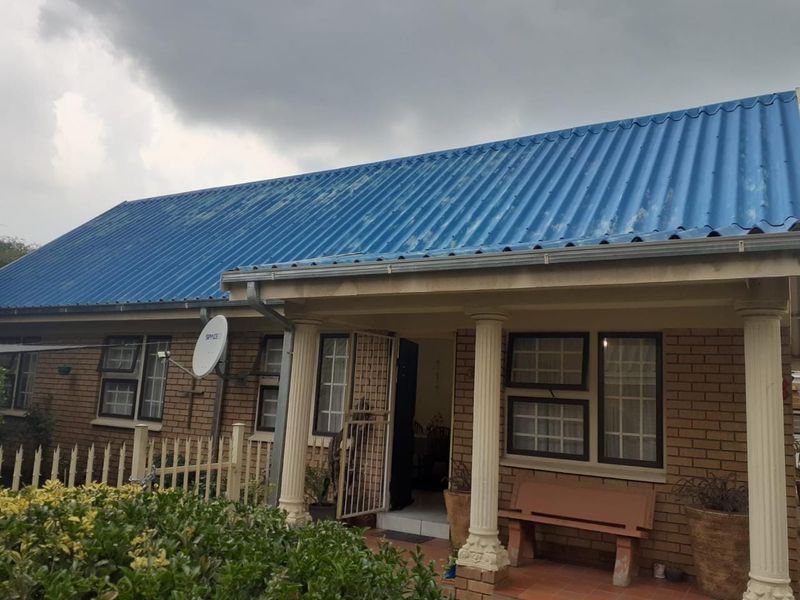 Front elevation of a townhouse featuring a corrugated metal roof, brick facade, and a covered porch area with decorative columns.