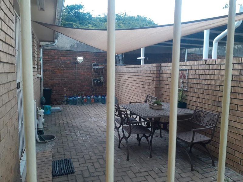 A paved outdoor patio area enclosed by brick walls, featuring a shade sail for cover and security bars.