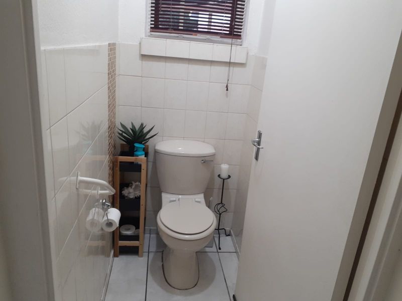 A compact guest bathroom featuring neutral ceramic wall and floor tiles, a standard toilet, and a small window with a venetian blind.