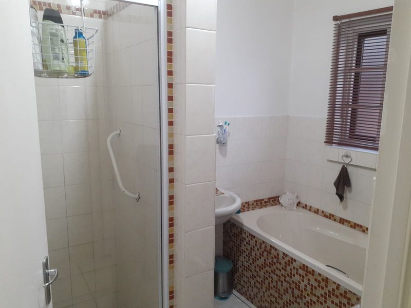 A functional bathroom featuring a shower enclosure with a grab rail, a pedestal basin, and a bathtub with decorative mosaic tile detailing.