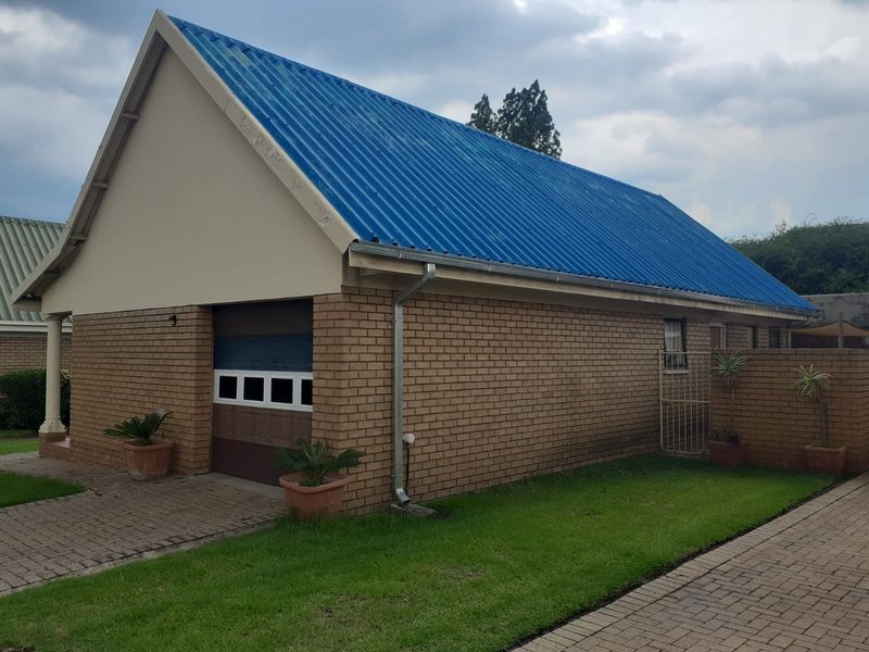 A detached brick garage featuring a blue corrugated metal roof and a paved driveway approach.