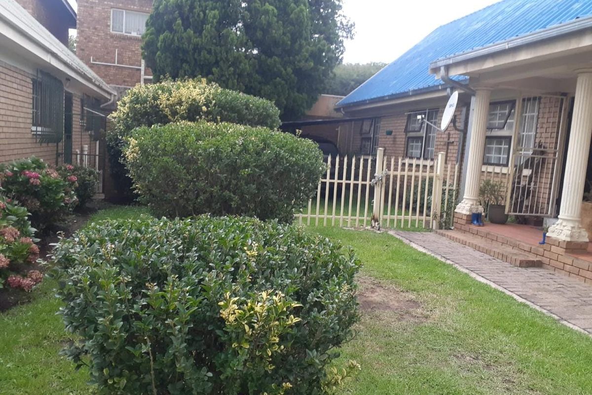 Rear exterior view of the townhouse featuring a small lawn, landscaped shrubs, paved walkway, and secure gated access.