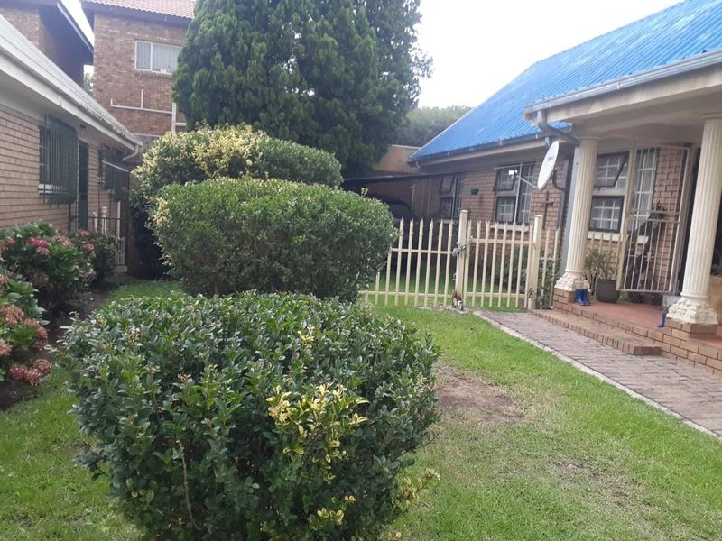 Rear exterior view of the townhouse featuring a small lawn, landscaped shrubs, paved walkway, and secure gated access.