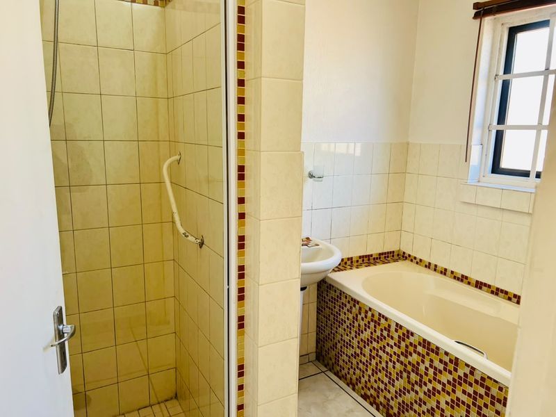 A functional bathroom featuring a shower enclosure, a bathtub with mosaic tile detailing, and a pedestal basin, offering a dated but practical layout.