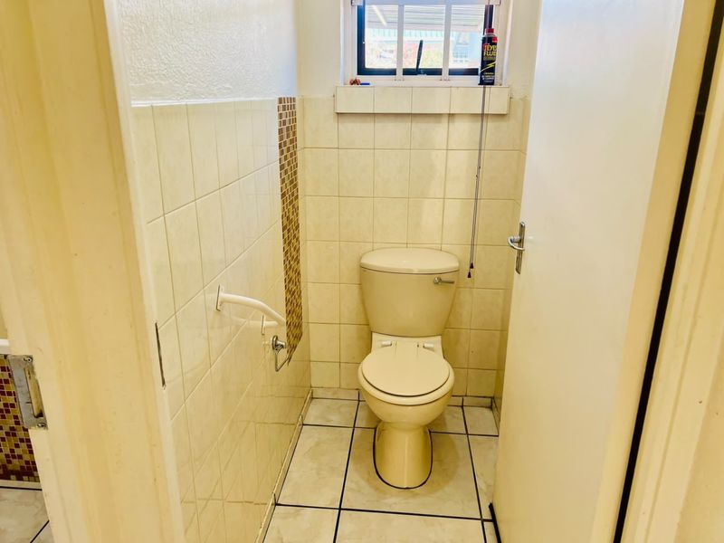 A compact guest bathroom featuring a standard toilet, ceramic wall and floor tiling, and a functional grab rail.