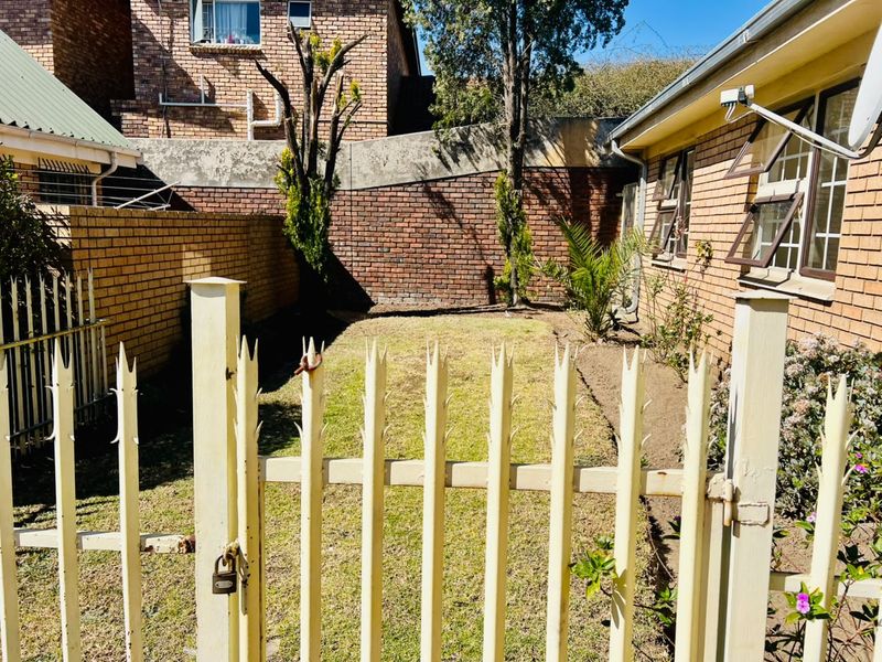 A rear exterior view of the townhouse featuring a small private lawn, enclosed by brick boundary walls and secured with a metal gate.