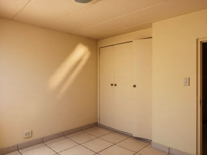 An empty bedroom featuring neutral tiled flooring and a built-in cupboard with sliding doors.