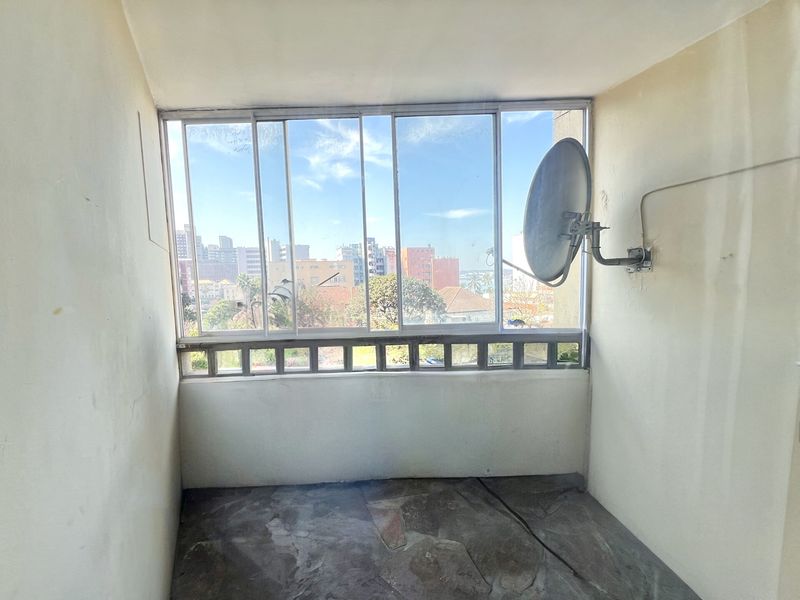 An enclosed balcony featuring stone flooring and large sliding glass windows with an urban view.