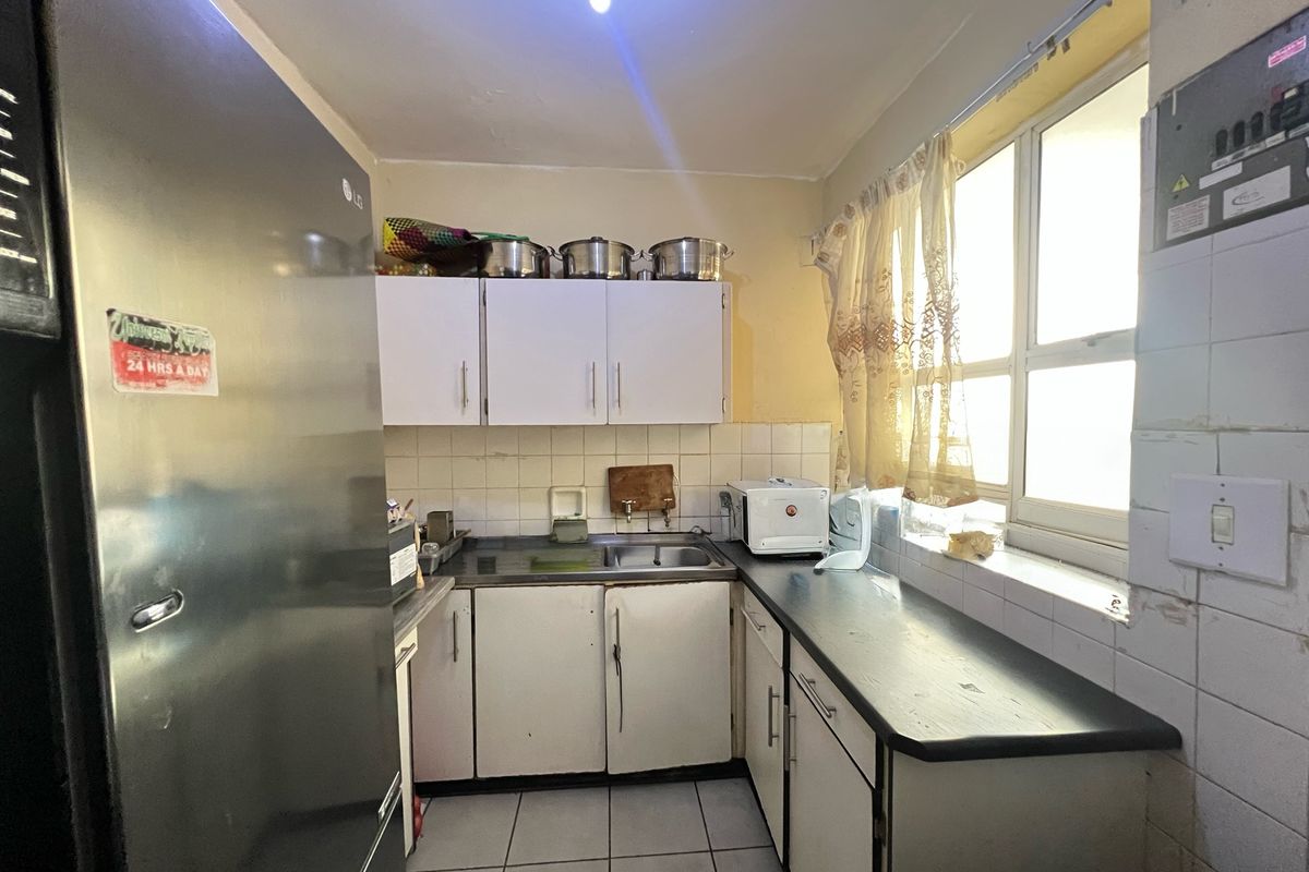 Compact kitchen featuring built-in cabinetry, a stainless steel sink, tiled backsplash, and tiled flooring, offering a functional layout in need of cosmetic updates.