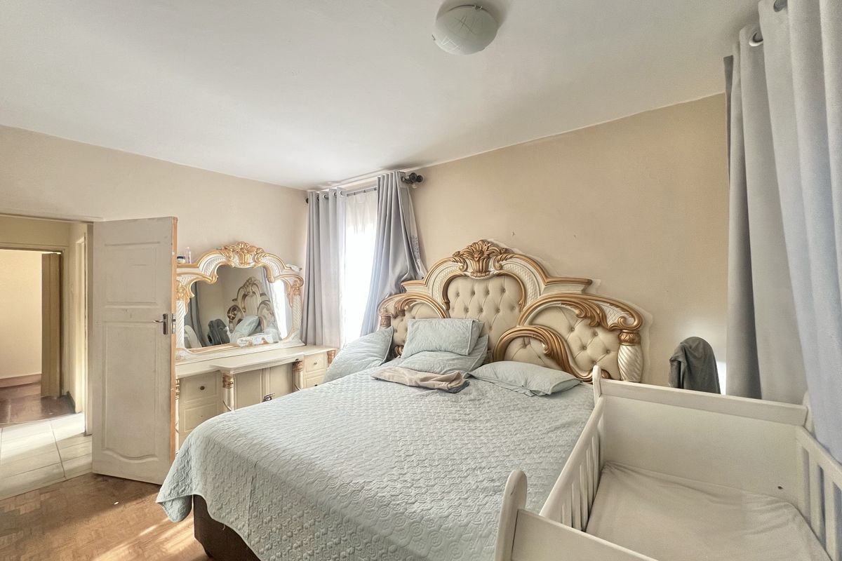 A bedroom featuring parquet flooring and neutral wall tones, offering a functional space with natural light from the window.