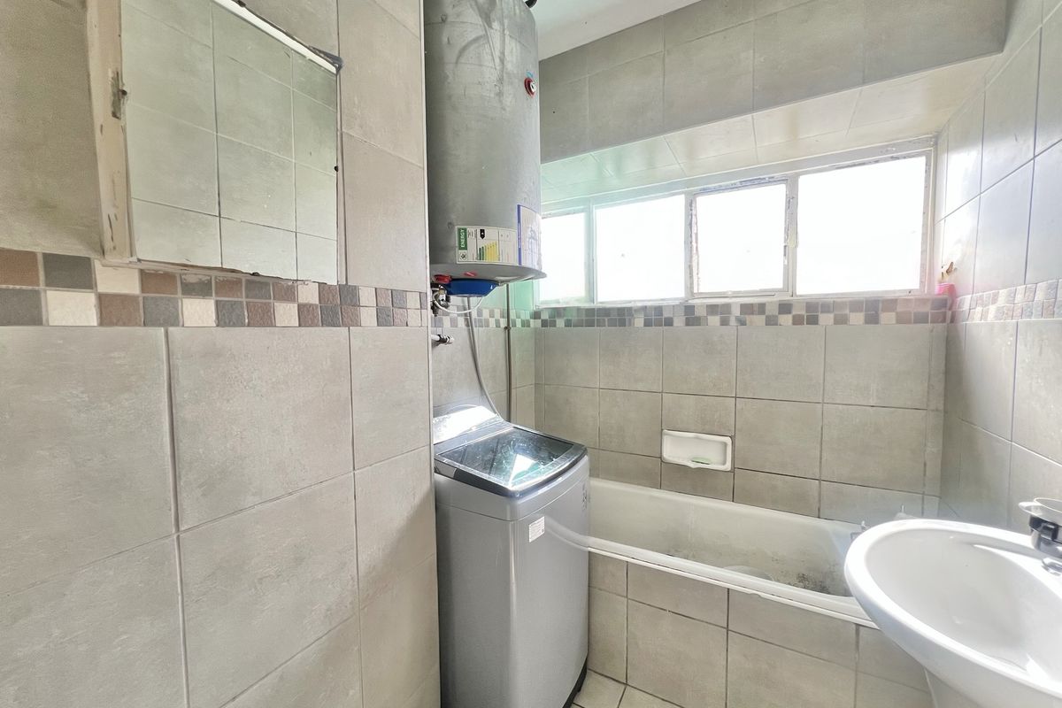 A functional bathroom featuring a bathtub, pedestal basin, and tiled finishes, currently housing a water heater and laundry appliance.