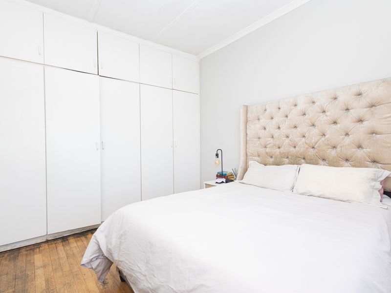 A bedroom featuring extensive floor-to-ceiling built-in cupboards and original hardwood flooring, offering a neutral canvas for potential interior updates.
