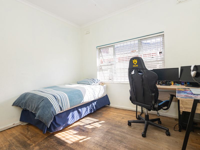 A functional bedroom featuring timber flooring and natural light through venetian blinds, suitable for use as a sleeping area or home office.