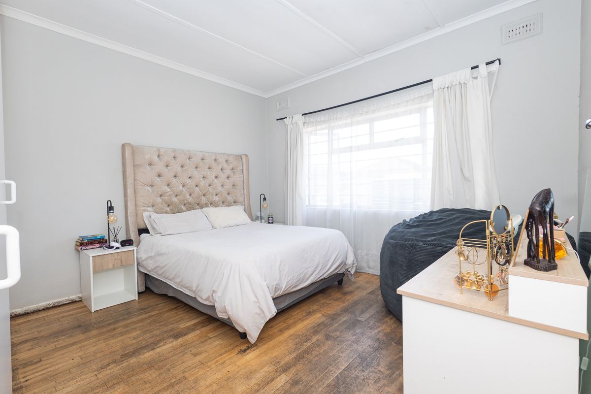 A well-lit bedroom featuring original timber flooring, neutral wall tones, and large windows allowing for ample natural light.