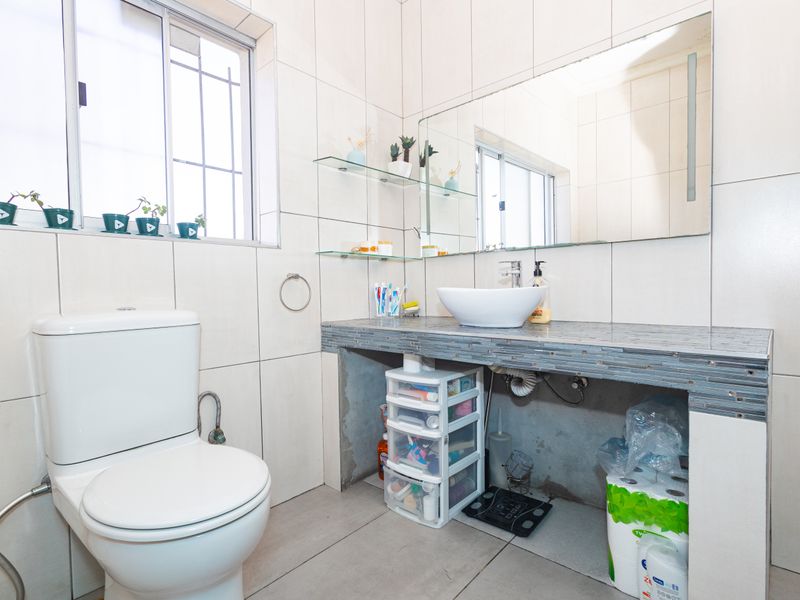 A functional bathroom featuring a vessel sink on a tiled vanity, wall-mounted mirror, and neutral ceramic tiling throughout.