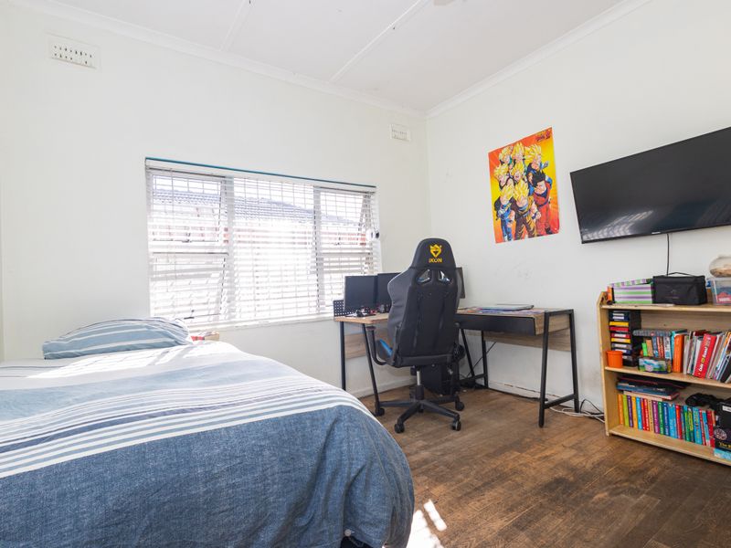 A functional bedroom featuring timber flooring, large window with venetian blinds, and wall-mounted television provision.
