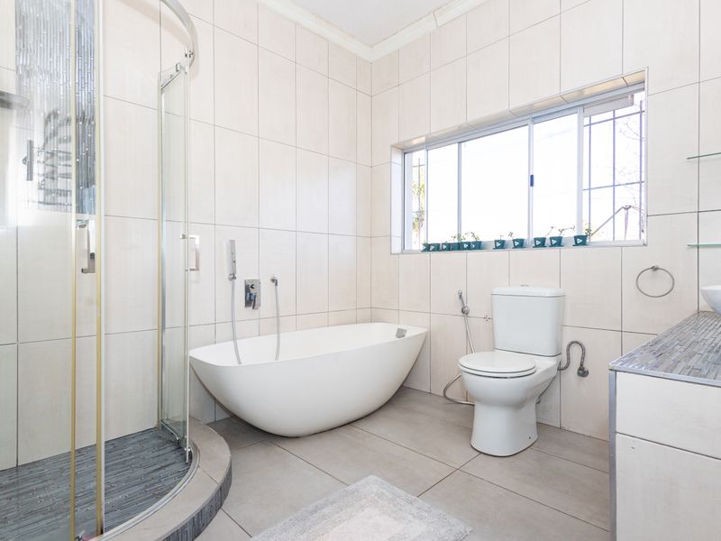 Modern bathroom featuring a freestanding bathtub, a separate curved glass shower enclosure, a vanity basin, and neutral floor-to-ceiling wall tiles.