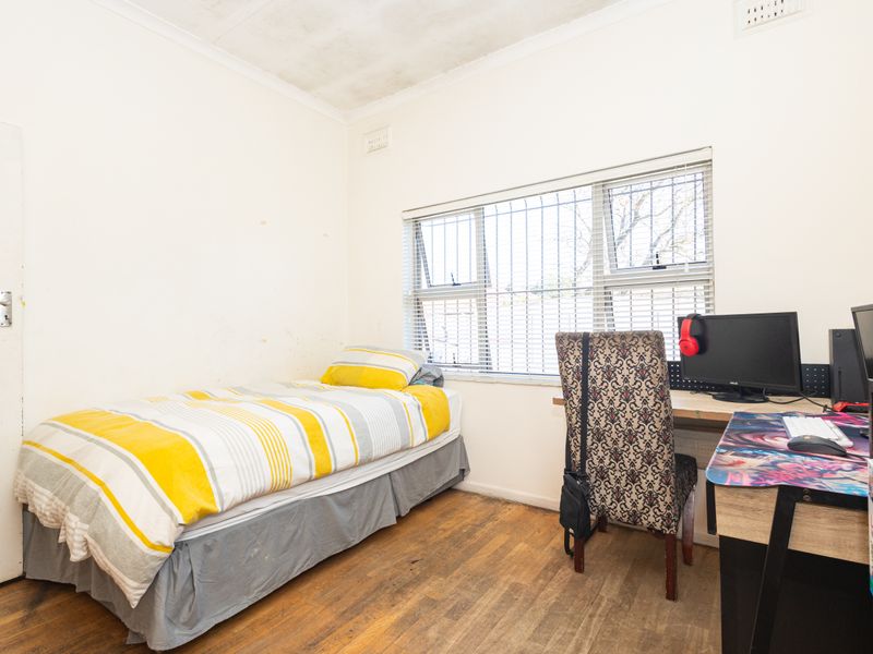 A bedroom featuring timber flooring, security bars on the window, and a ceiling with visible staining, requiring cosmetic updates.