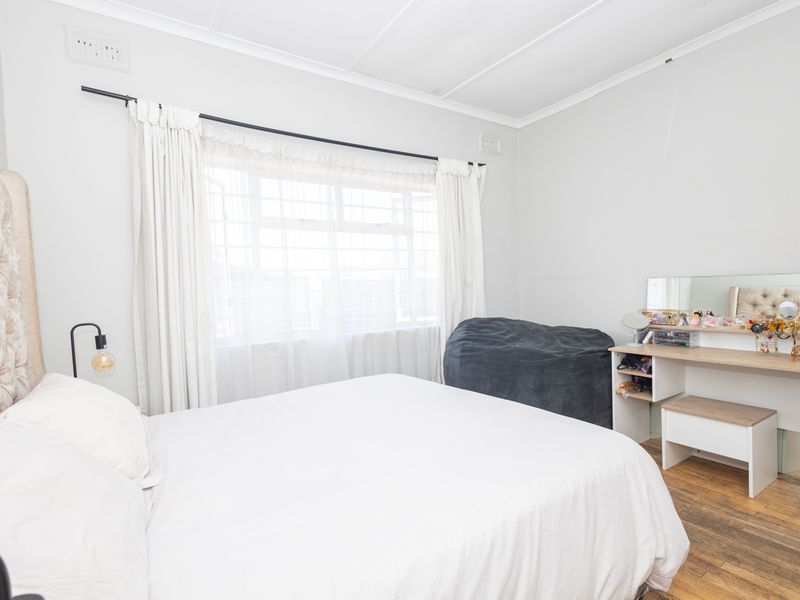A bright bedroom featuring timber flooring, a large window with curtains, and neutral wall finishes.