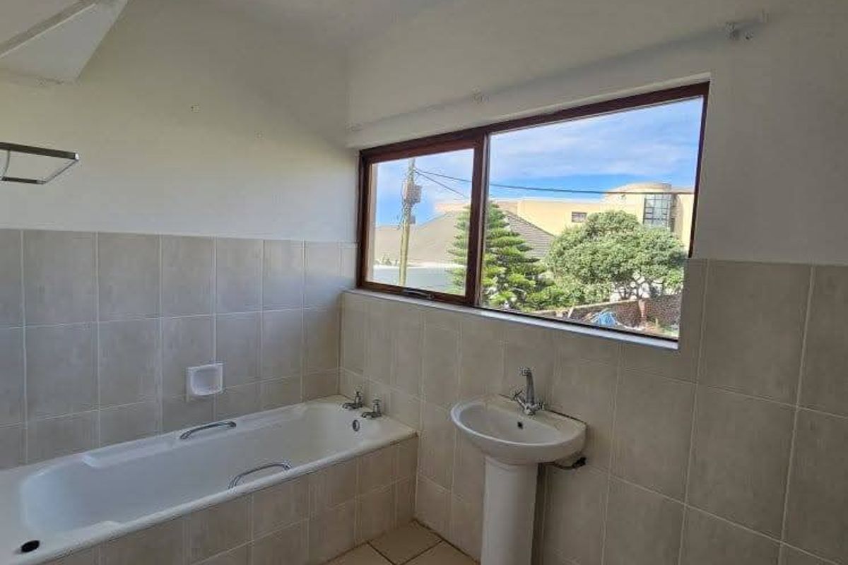 A functional bathroom featuring a built-in bathtub, pedestal basin, and neutral ceramic tiling throughout, offering a clean and simple layout.